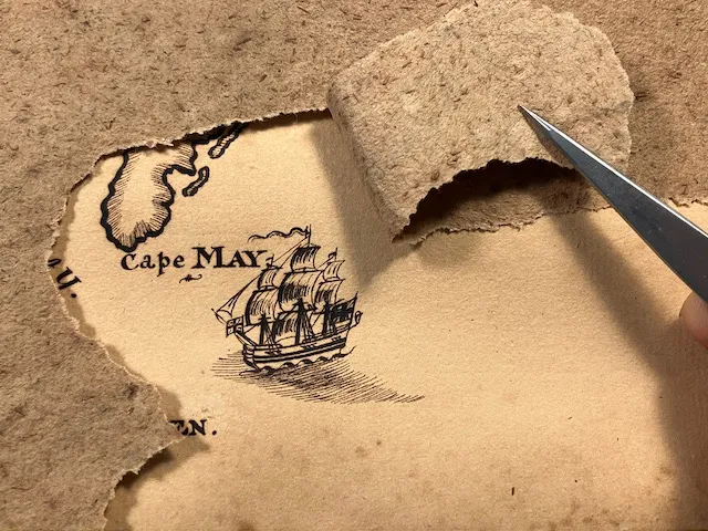 tweezers pulling back acidic paper from an ink drawing hidden below