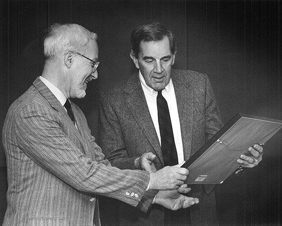 Ernie Prudente and another man look at a framed paper together.