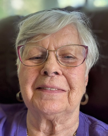 Woman with short grey hair and glasses smiles at the camera.