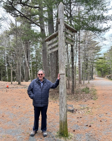 Man stands next to a directional sign in the forest.