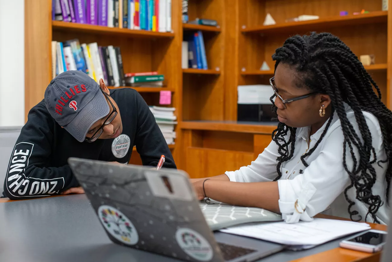 Student writes notes while other student works at computer