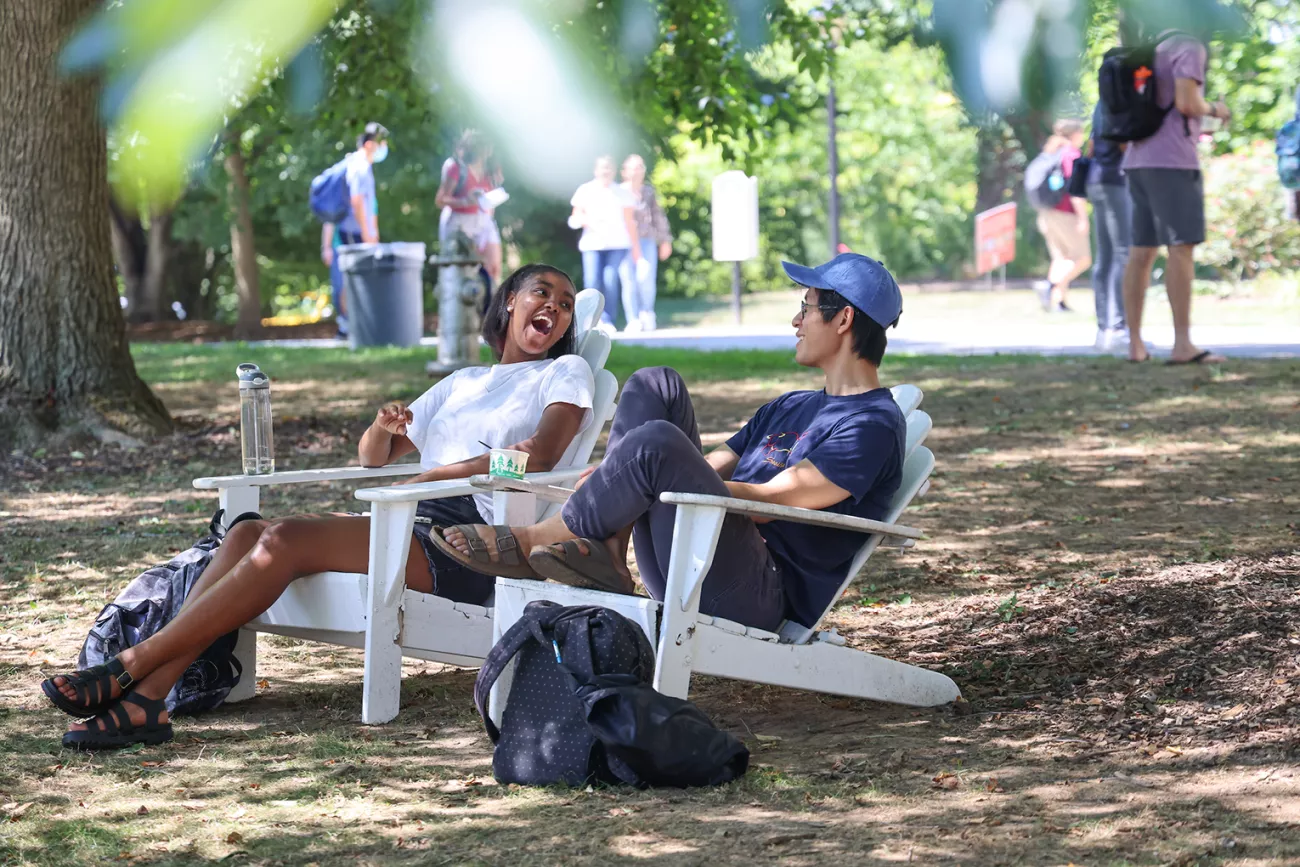 Students sitting on white Adirondack chairs outside