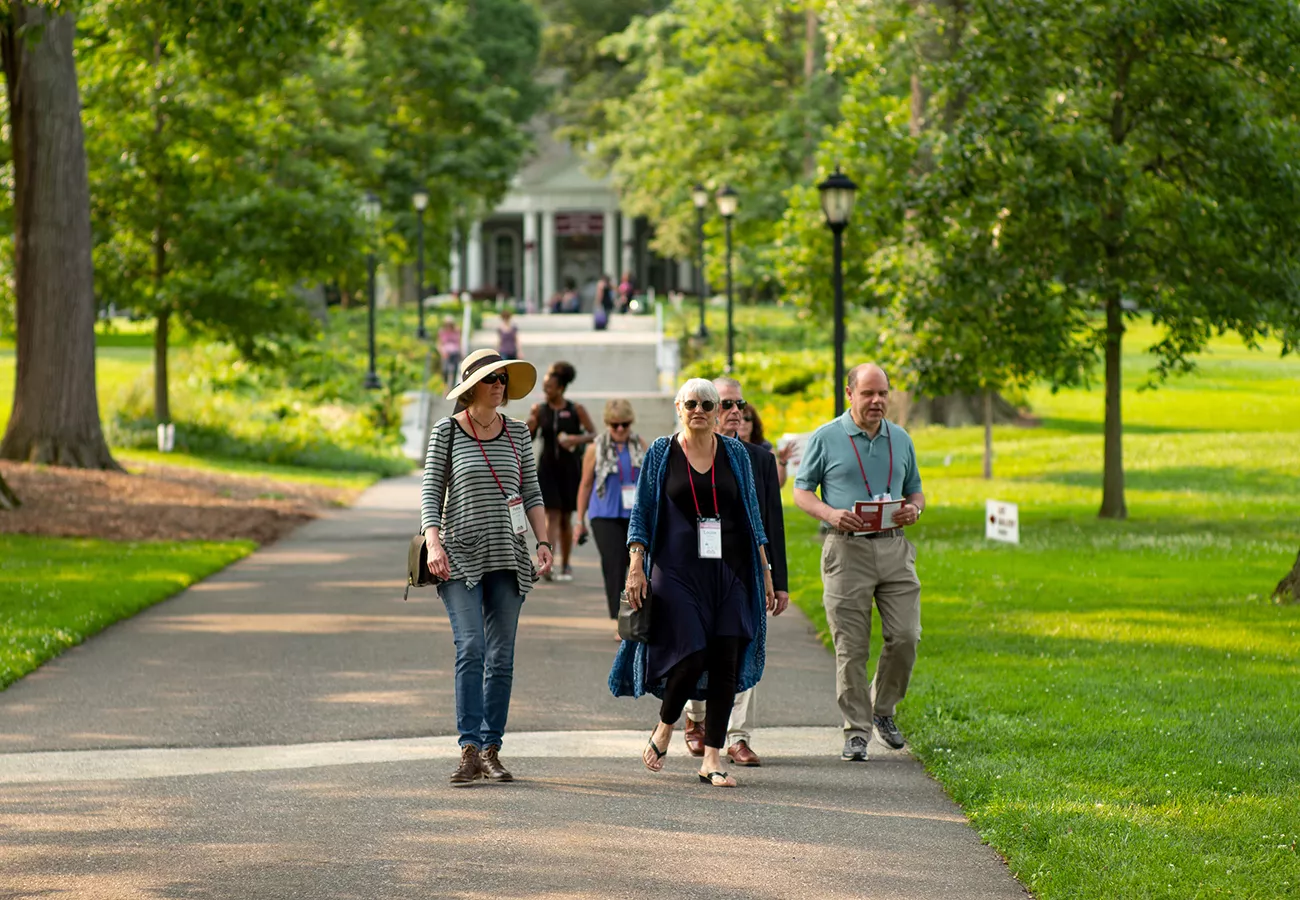 People walk outdoors among trees with Parrish Hall in background