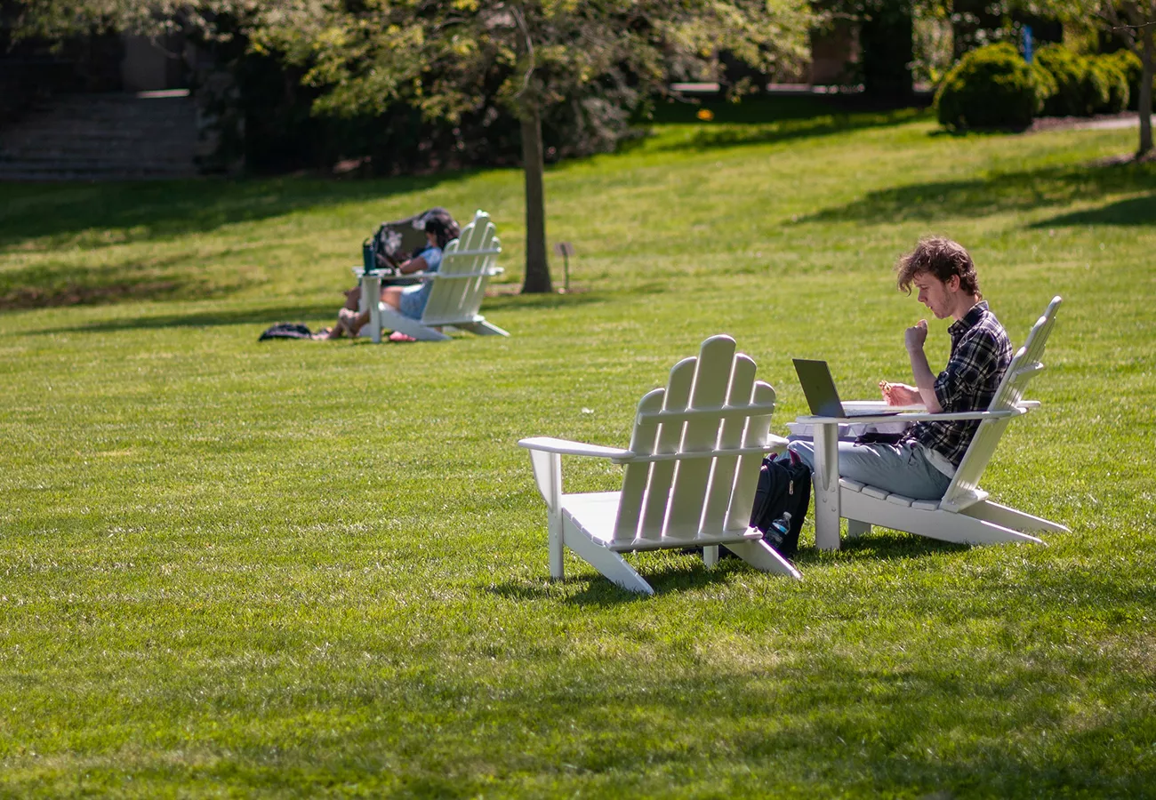 Students sits on grass in white chair