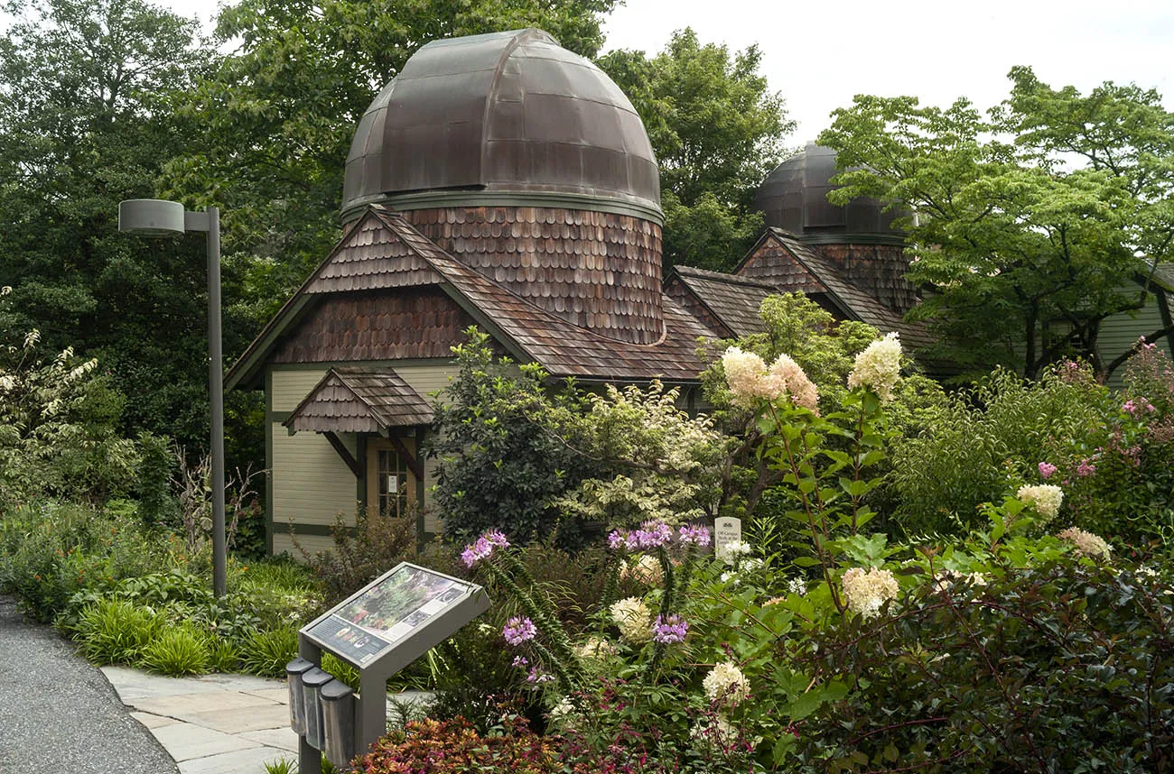 A shingled dome roofed observatory surrounded by flowers