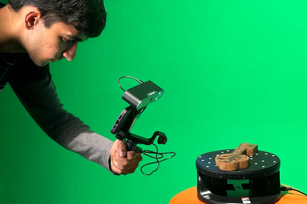 Student scans wooden key in front of a green screen for modeling