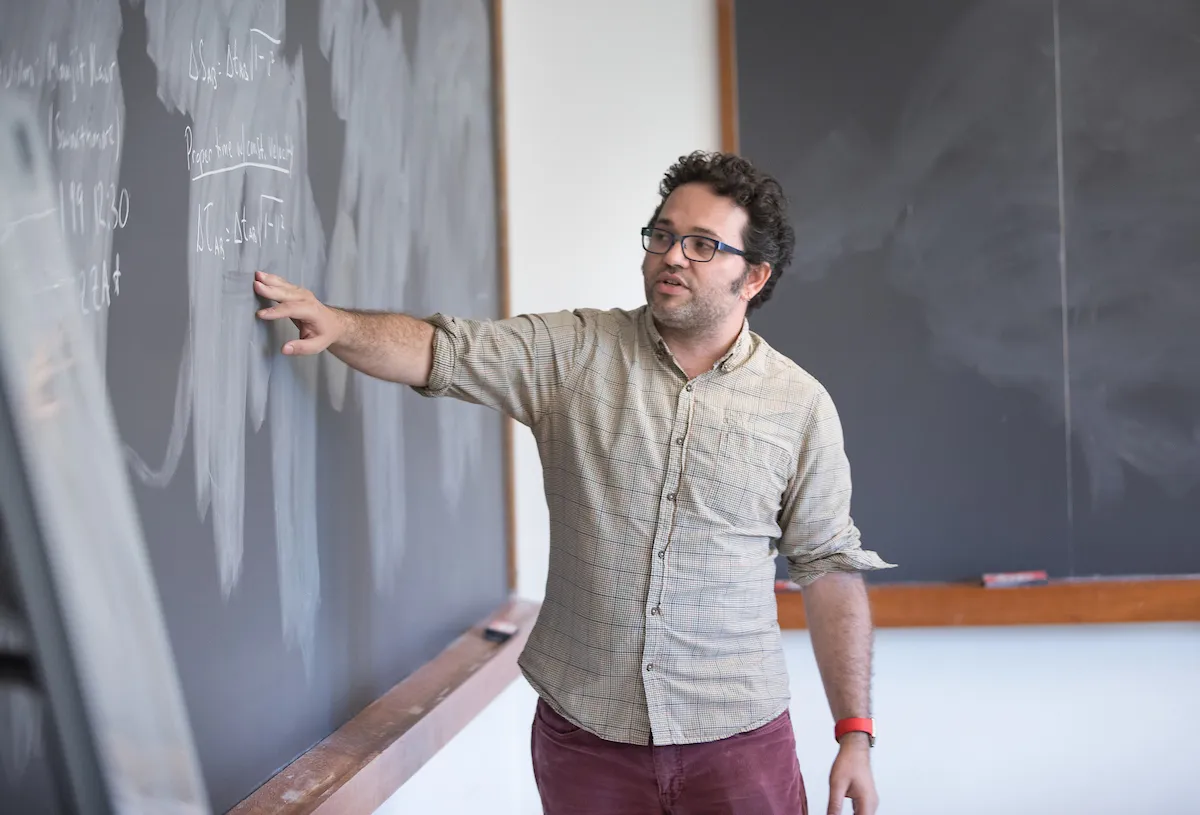 Photo of Tristan Smith pointing at a blackboard.