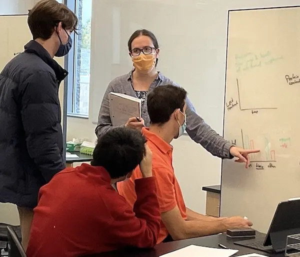 Carolyn Bauer in a facemask at a whiteboard teaching 3 students