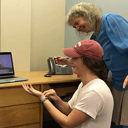 A woman uses sign language while another woman looks on over her shoulder