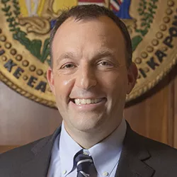 Portrait of Josh Green smiling in front of state seal of Hawaii