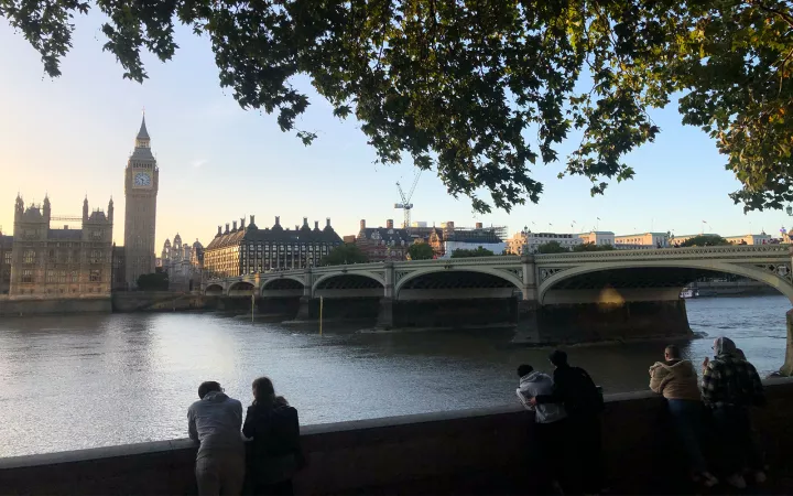 People leaning over wall facing river, bridge, and city with clock tower