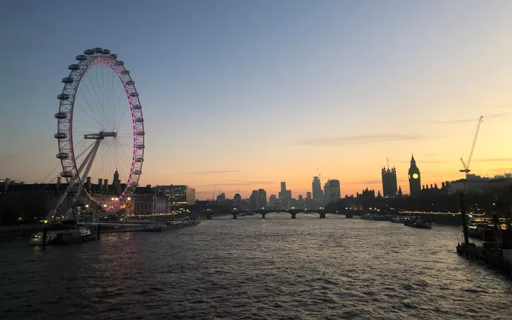 River with city in distance and Ferris Wheel with pink lights on one side