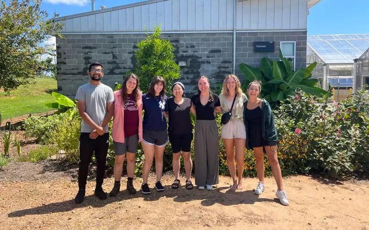 Group standing outside in front of crops and greenhouses