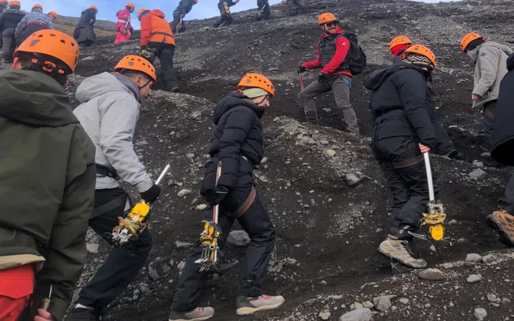 People with orange helmets climbing rocky surface