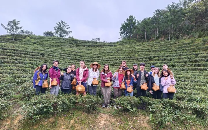 Students standing on farmland with woven hats and pouches