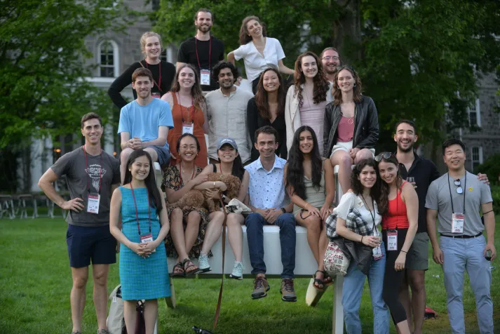 Large group of alumni pose on oversized Adirondack chair