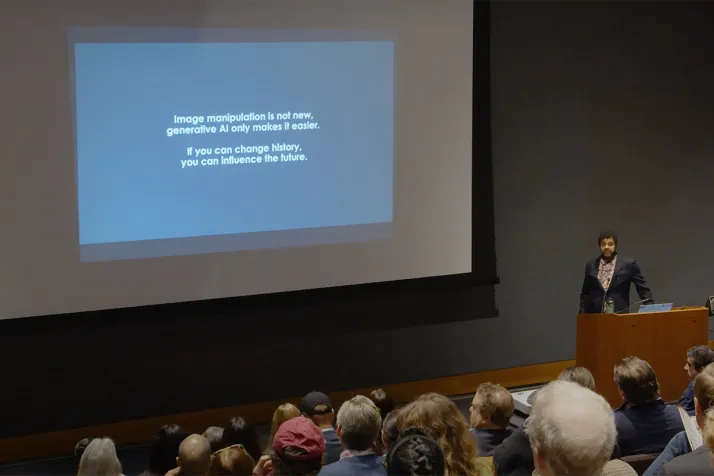 Person delivers lecture in front of projector screen that reads "Image manipulation is not new, generative AI just makes it easier"