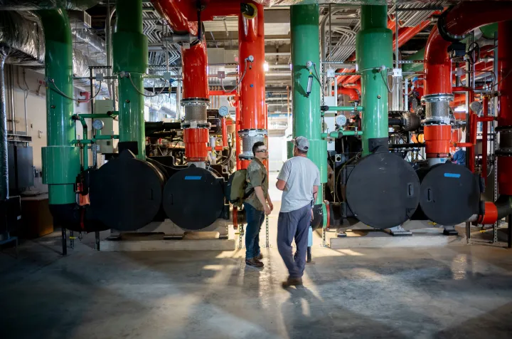 Person looks at large green and ride pipes during tour of geothermal exchange