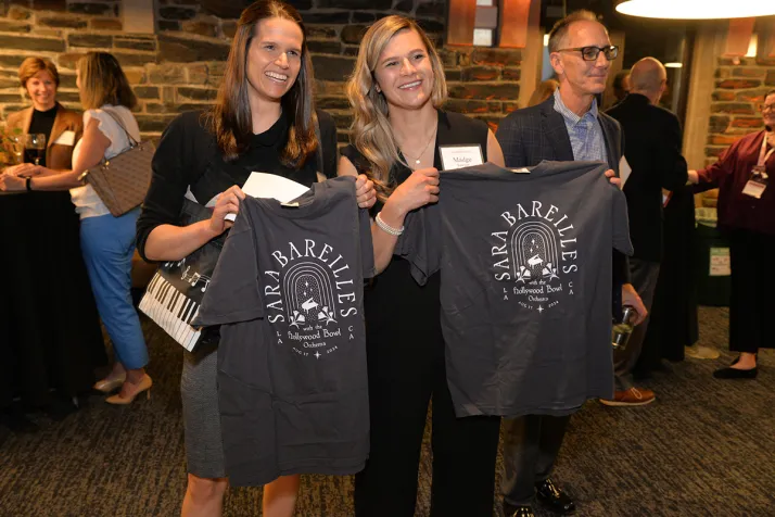 Two people hold up t-shirts with "Sara Bareilles" on the back of them