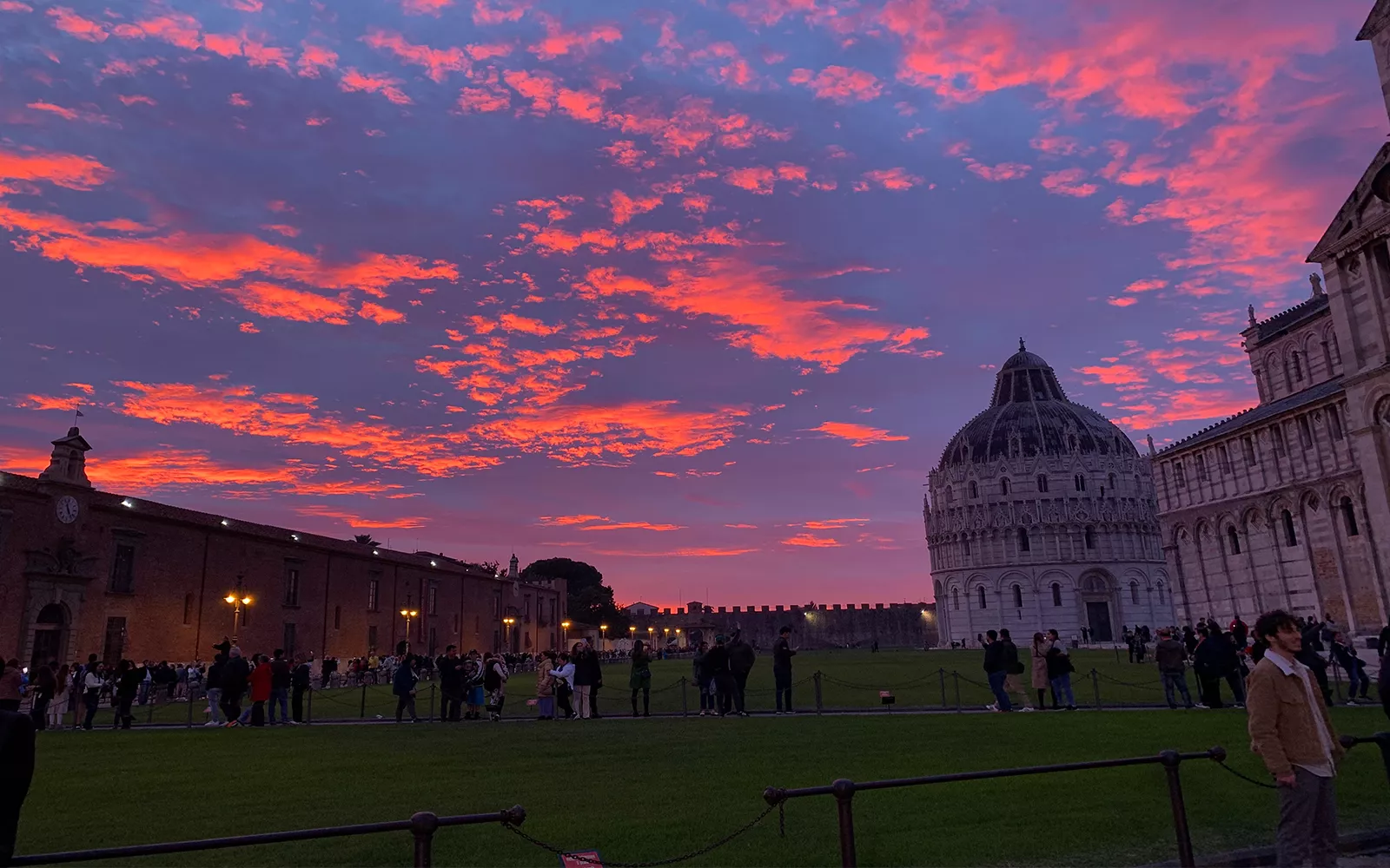 Dark blue sky with bright pink clouds over scene with people walking between buildings