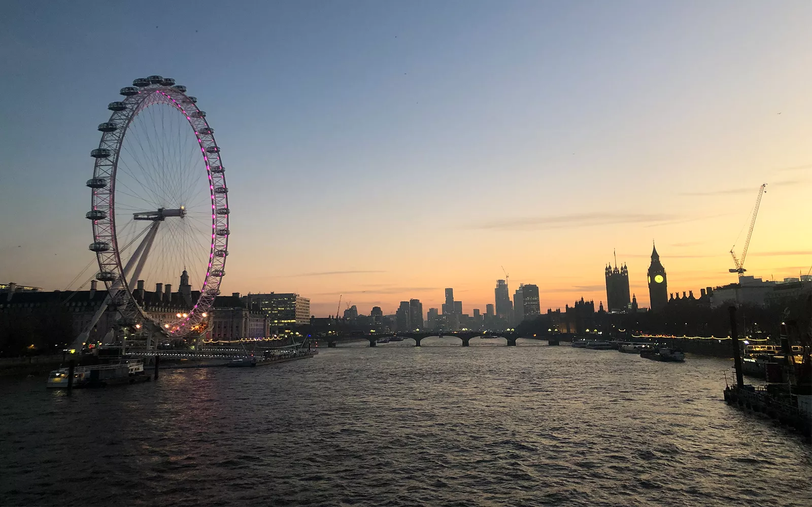 River with city in distance and Ferris Wheel with pink lights on one side