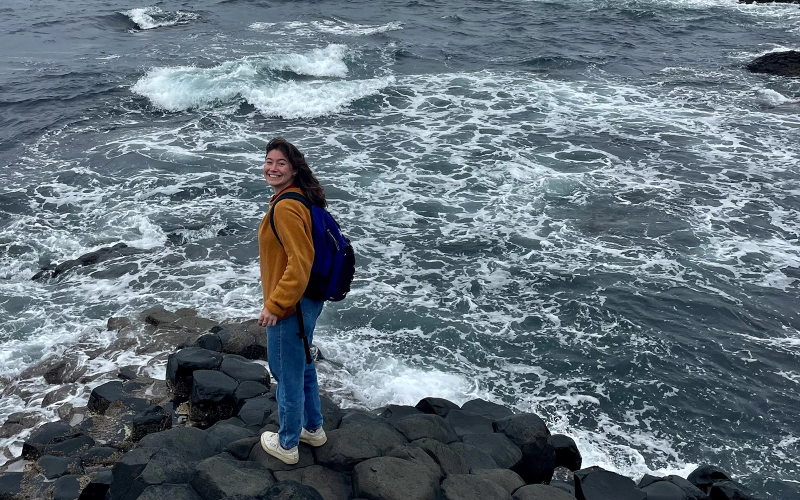 Person standing on rocks in front of frothy waves