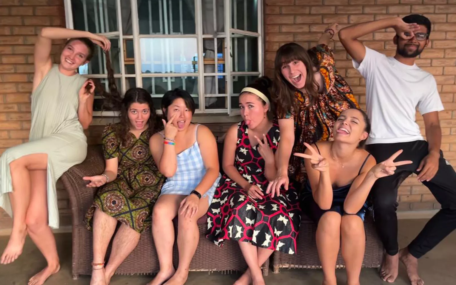 Group of students sitting on an outdoor couch making silly gestures and expressions