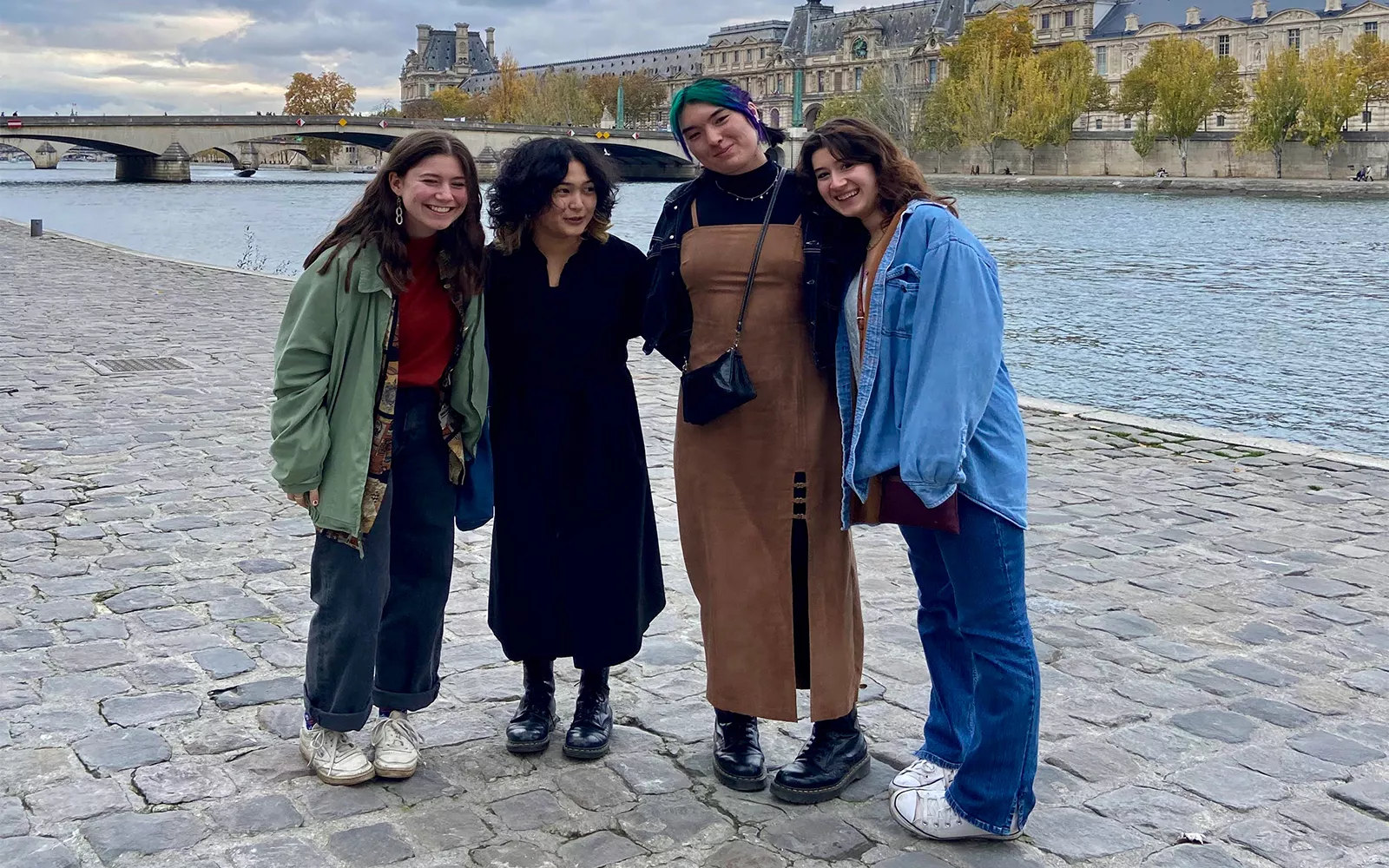 Students standing on cobbled path in front of river and bridge