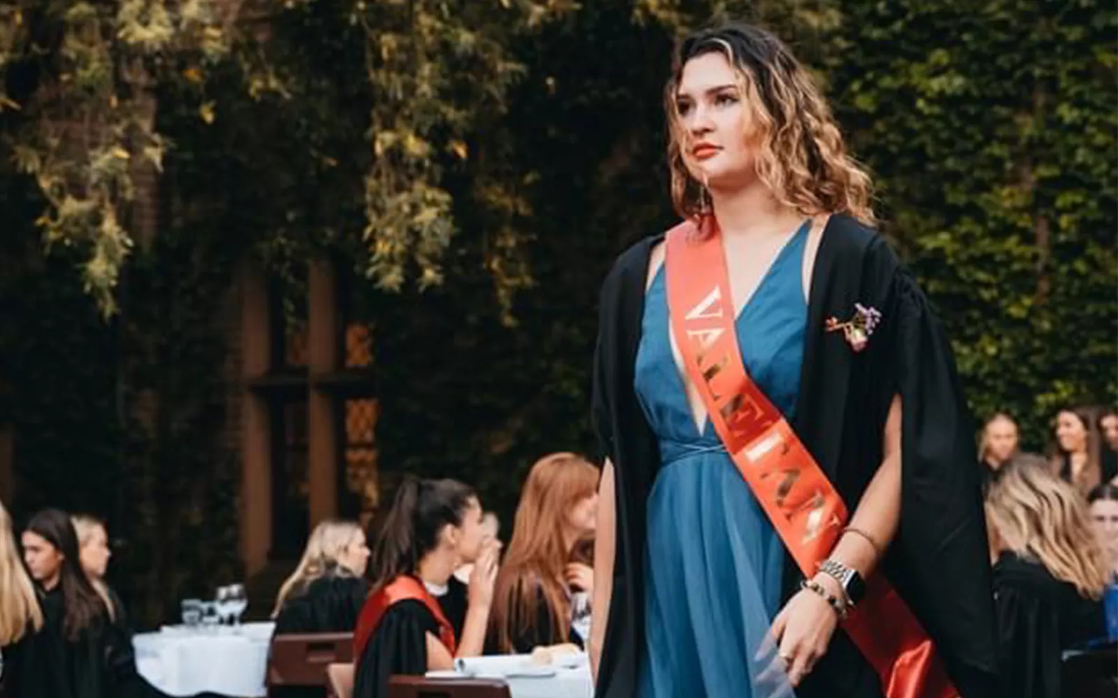 Student wearing sash and robe walking forward in front of audience