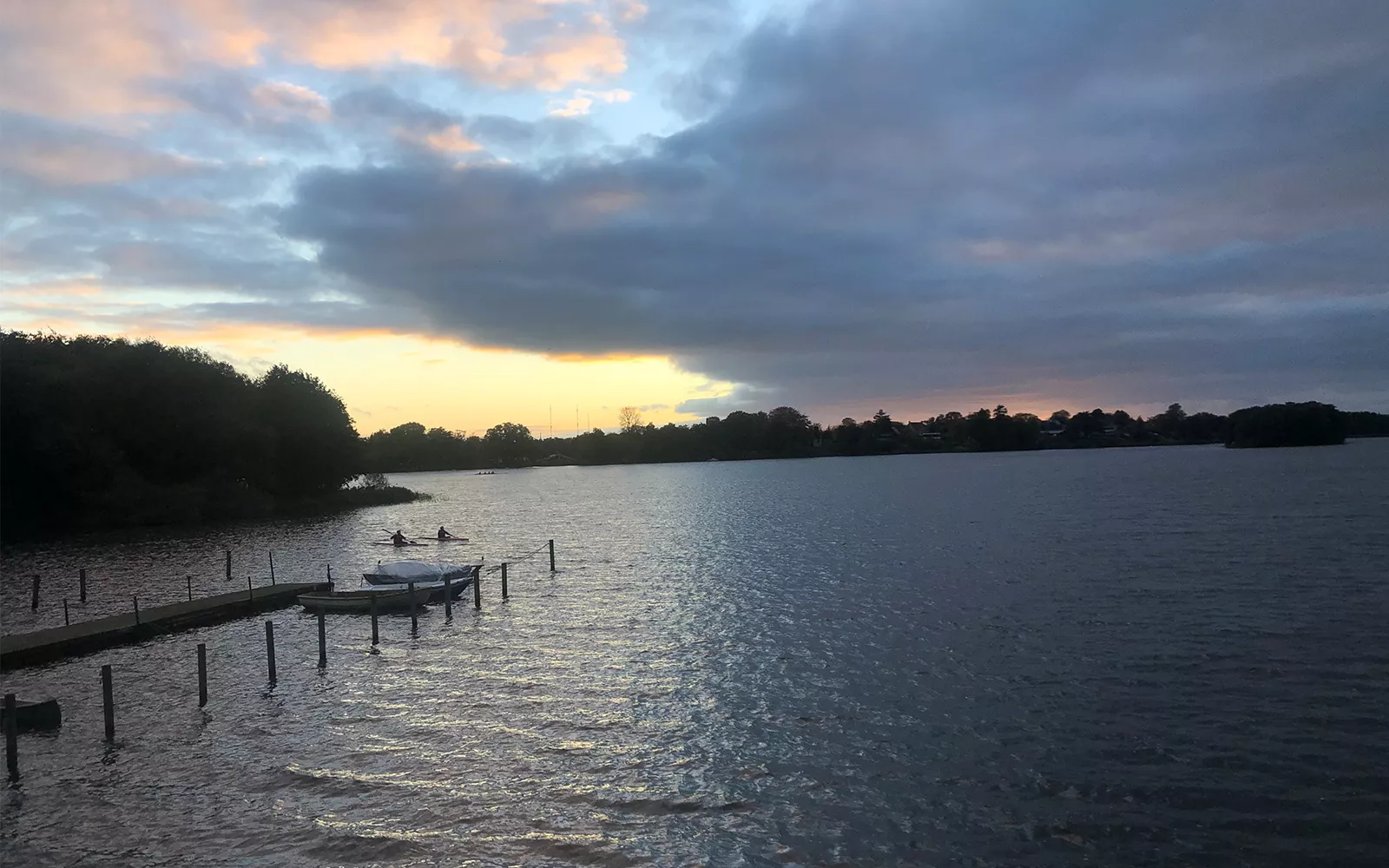 Small figures in kayaks on large body of water with reflection of orange-tinged sky