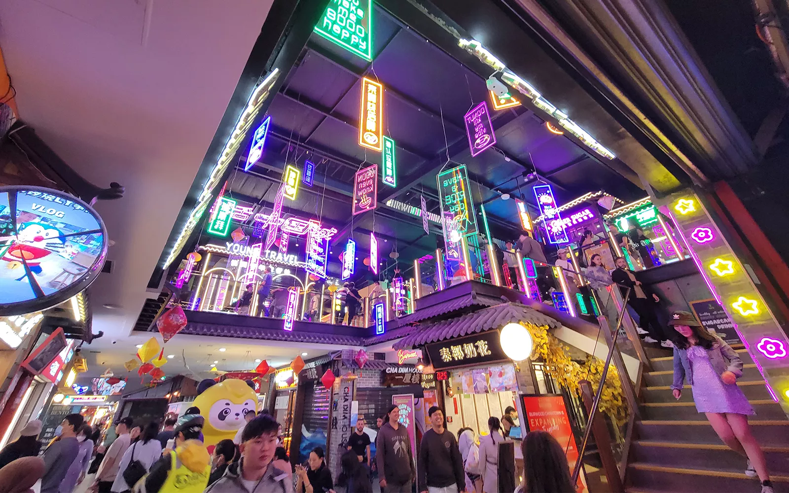 People walking through shopping mall with neon signs