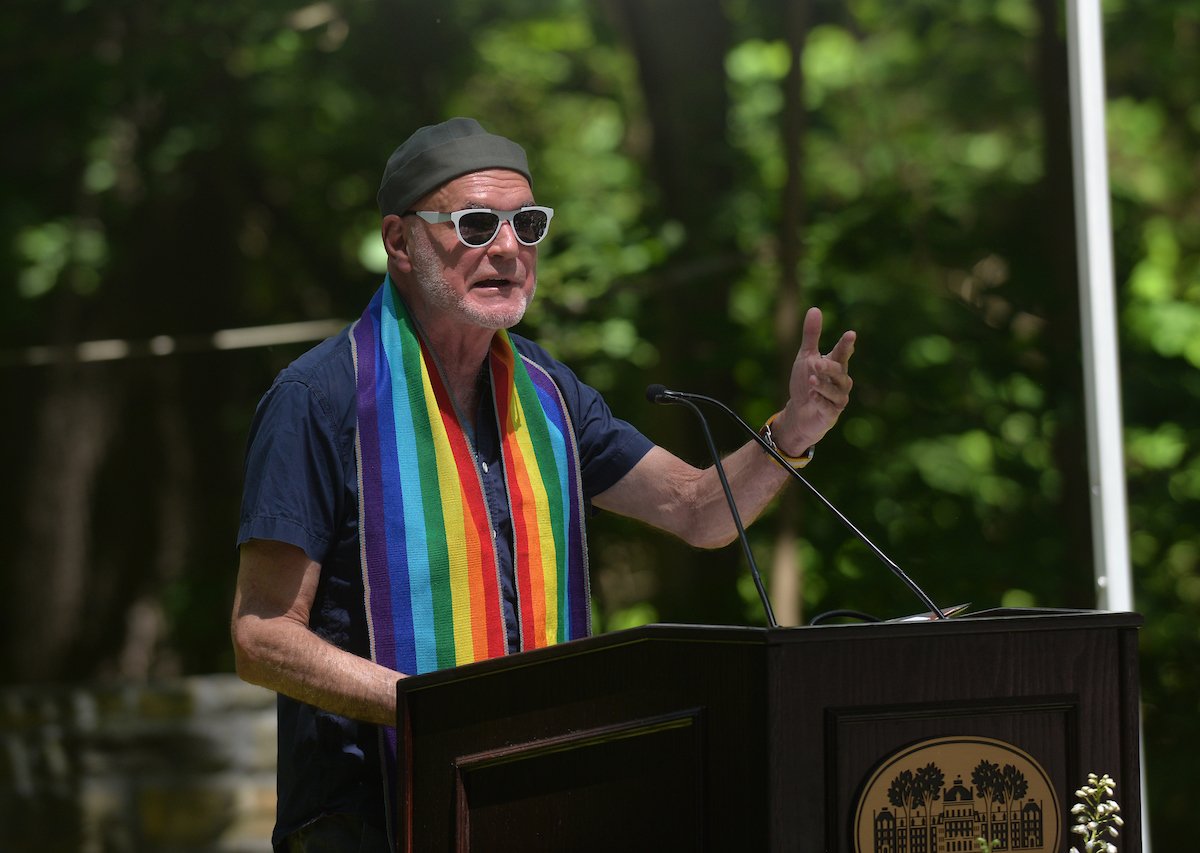 Richard Sager wears rainbow scarf and speaks at podium during alumni collection