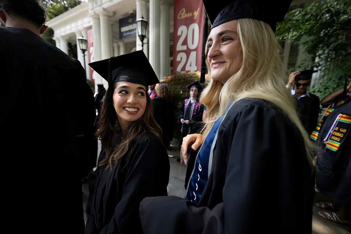 Two students wearing caps and gowns line up for baccalaureate