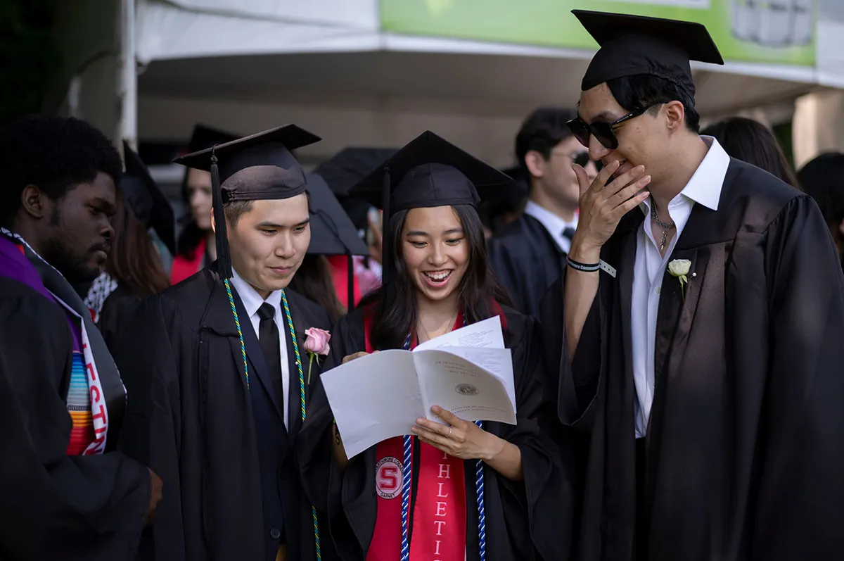 Students wearing cap and gown examine commencement program