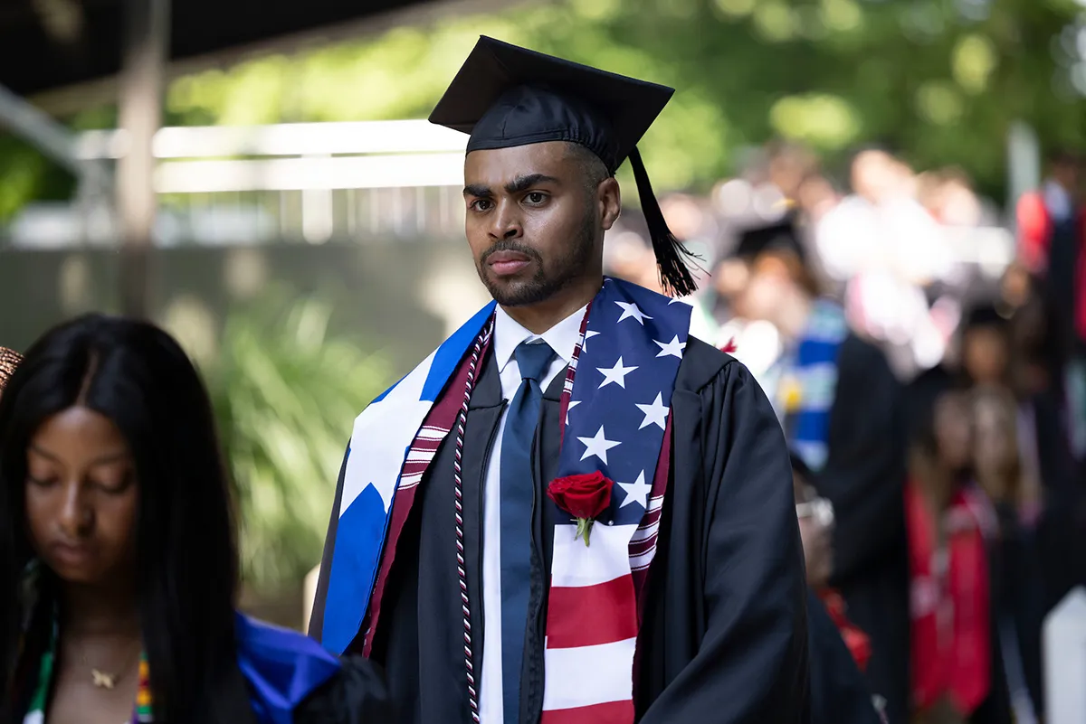 Student wearing flags draped on shoulder walks during commencement procession