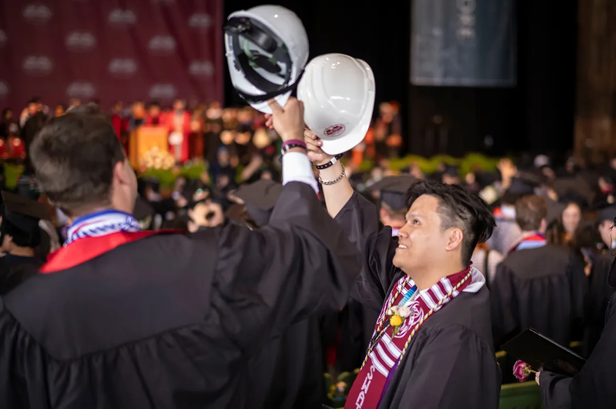 Students bump white construction helmets together in celebration