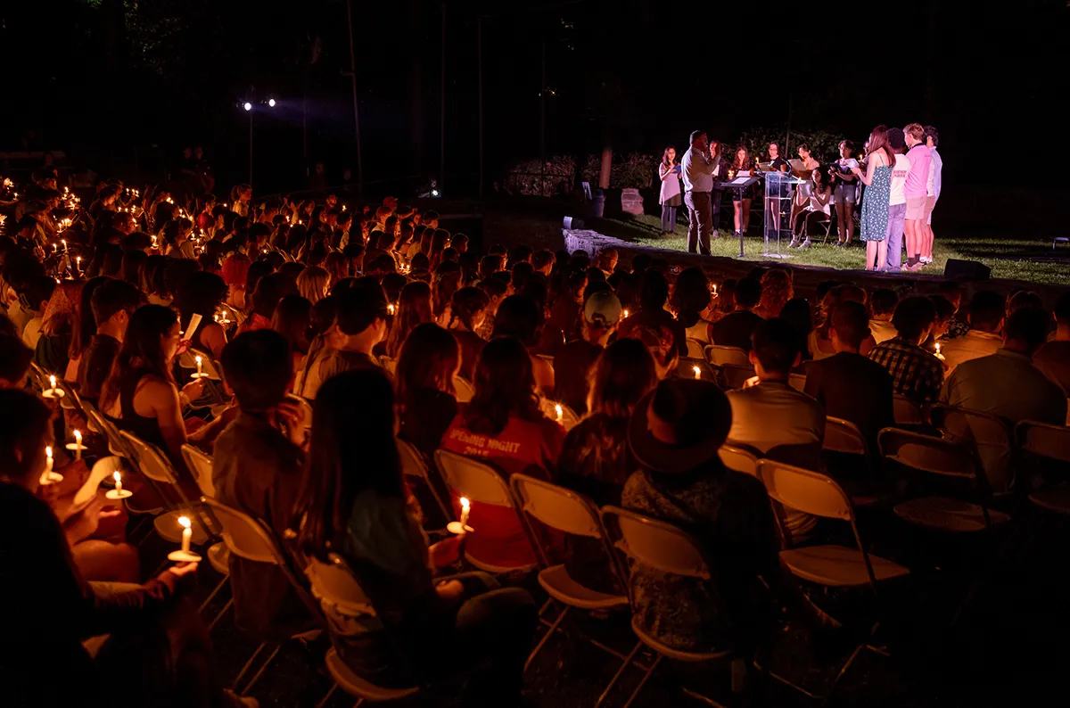 Students hold candles in outdoor amphitheater during Last Collection