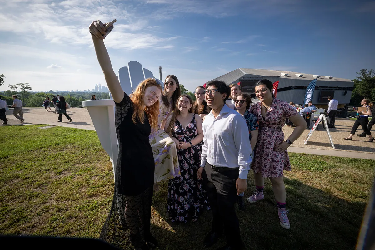 Students take a selfie in front of large white Adirondack chair