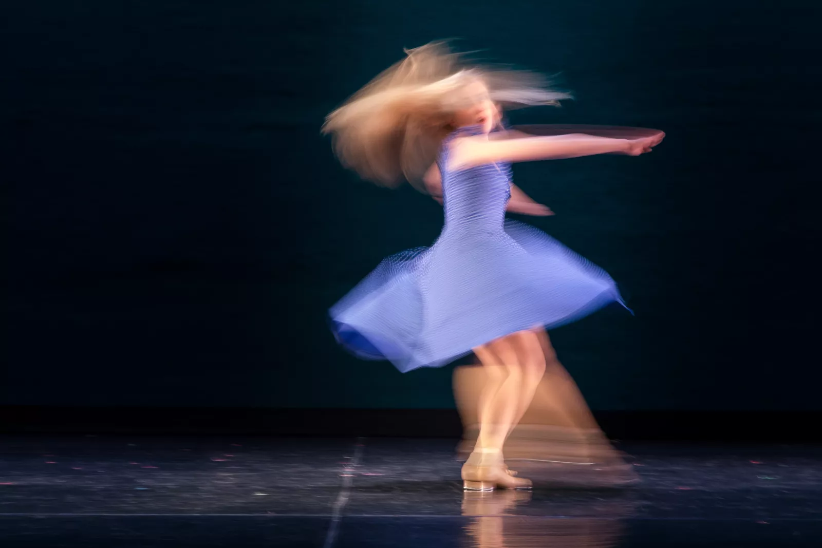 A tapper spins in a blue dress, blurry