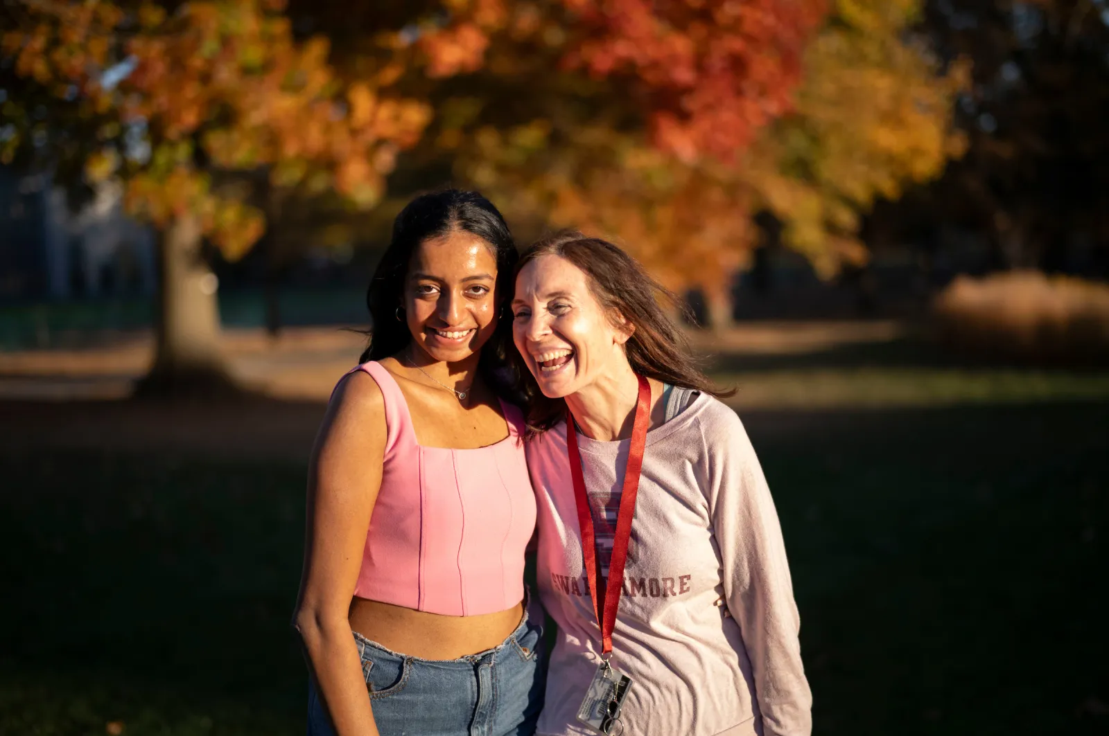 Two people pose for picture in front of multicolor tree in autumn