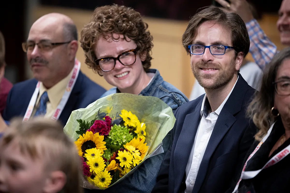 Two people sit next to each other with a bouquet of yellow flowers in between them