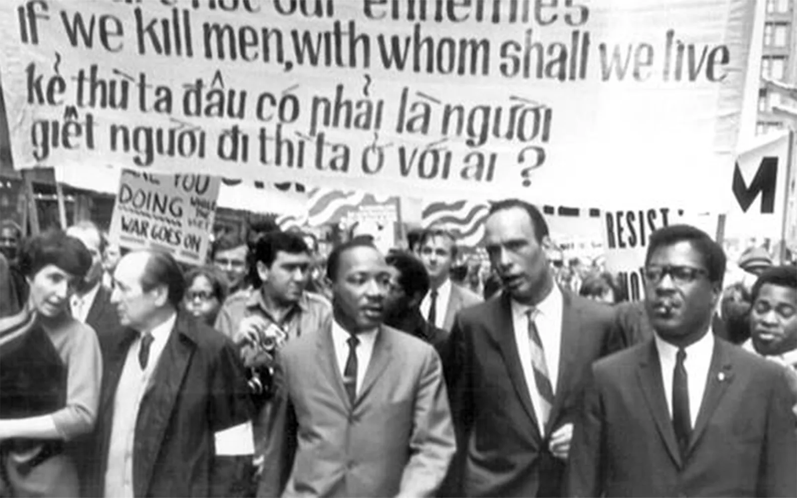 MLK marching peacefully with other leaders, with a placard behind them reading, "If we kill men with whom shall we live" in both English and Vietnamese.