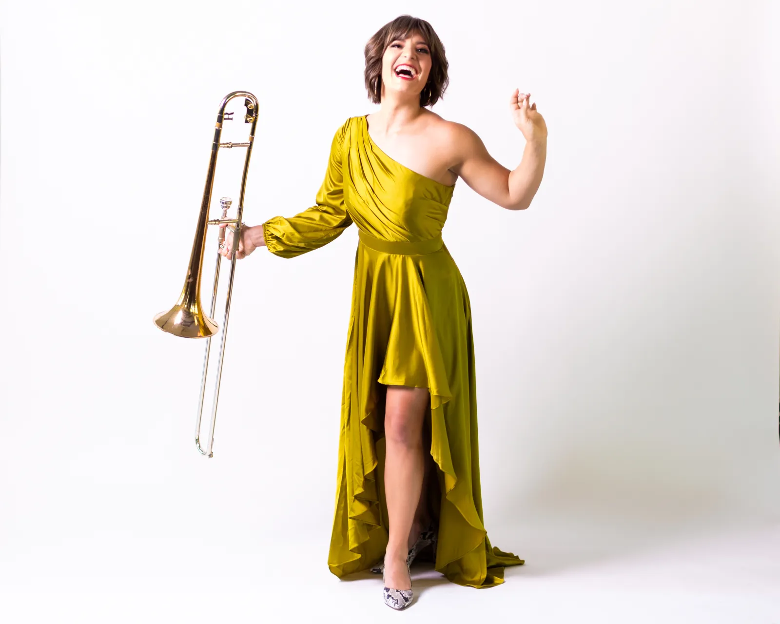 Aubrey Logan standing against a white background wearing a gold gown holding a trombone