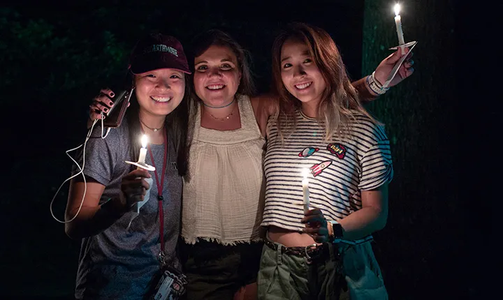 Three students hold candles facing camera