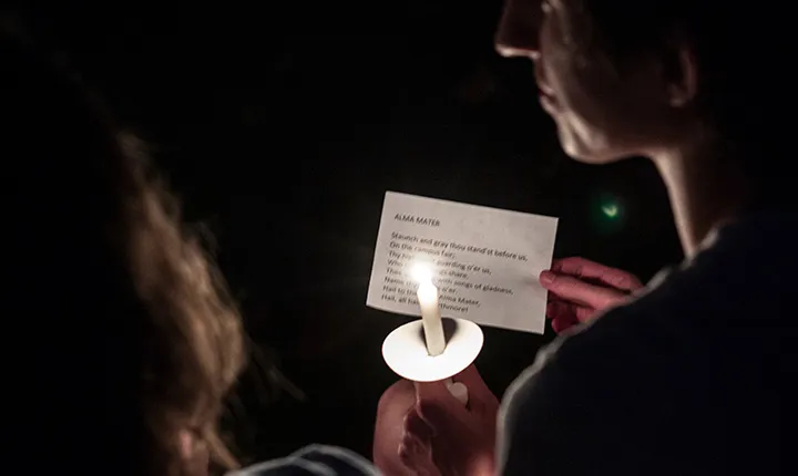 Student holds candle and copy of alma mater.