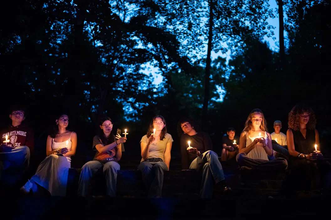 Students sit on wall and hold candles during First Collection