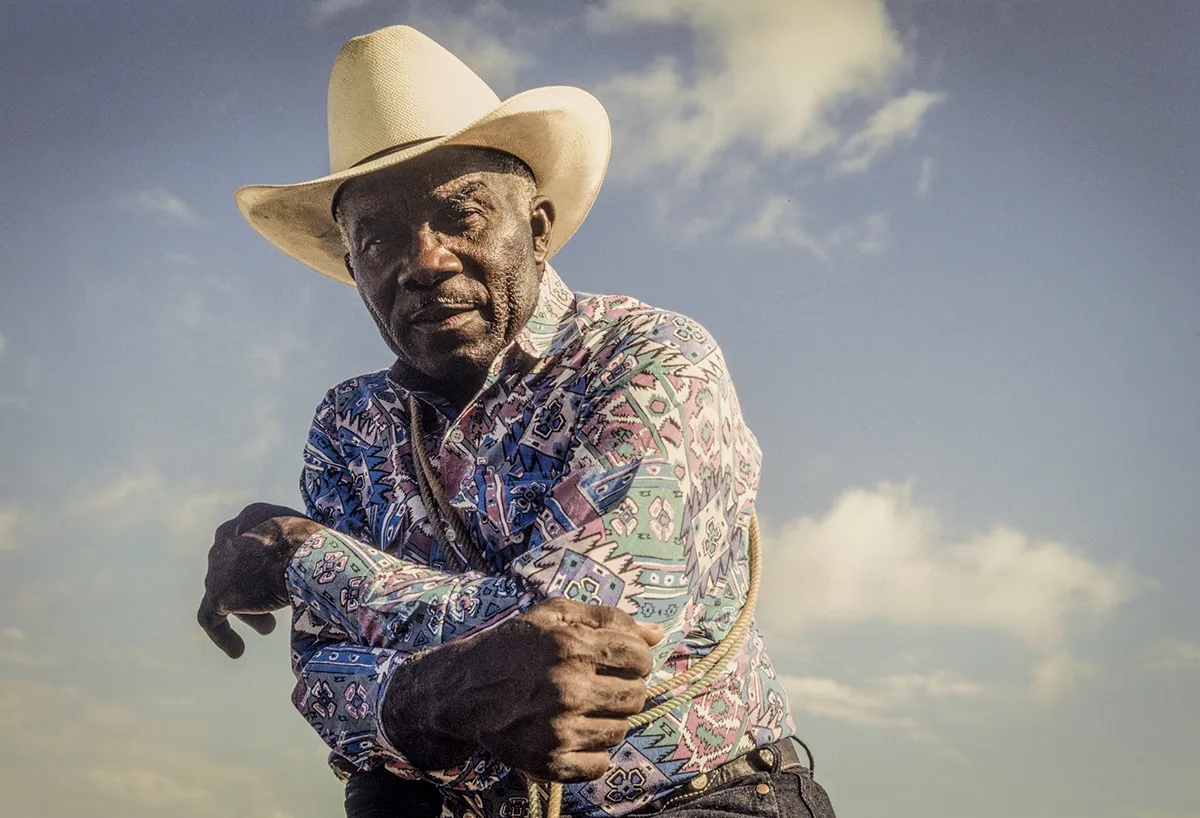 Black cowboy stands in front of blue sky with white clouds