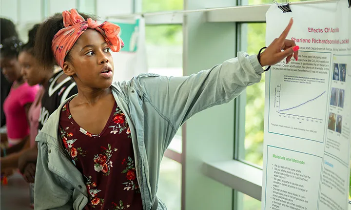 Girl points to poster at science fair