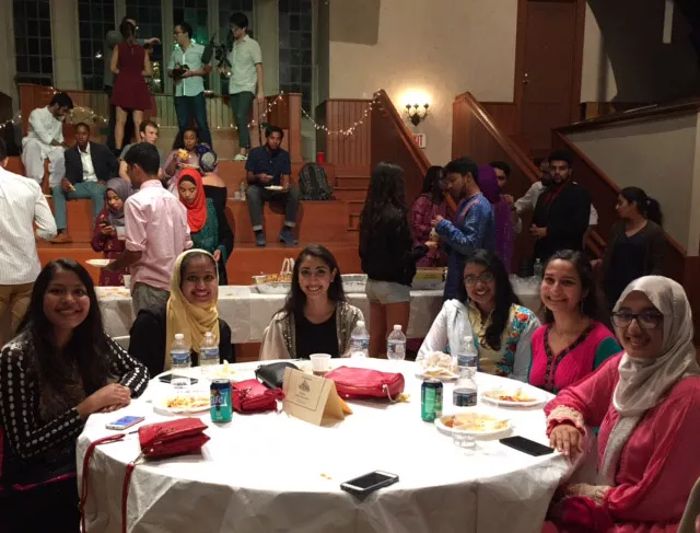 Students smile, sitting around a table during the Eid Banquet