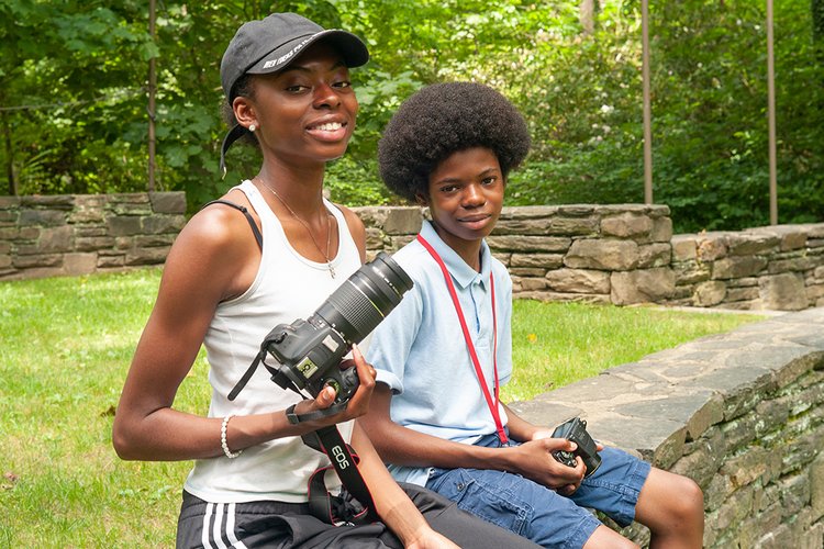 Two students sit outside with digital cameras